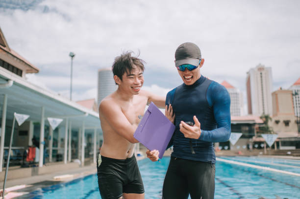 happy Asian chinese personal trainer analysis showing his student record breaking on stopwatch the swimming exam result at pool side after education training class Asian chinese personal trainer analysis showing his student on the swimming exam result at pool side after education training class record breaking stock pictures, royalty-free photos & images