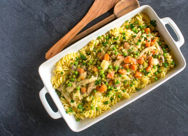 Pasta with chicken meat, sauce and vegetables in a casserole on dark table background with copy space