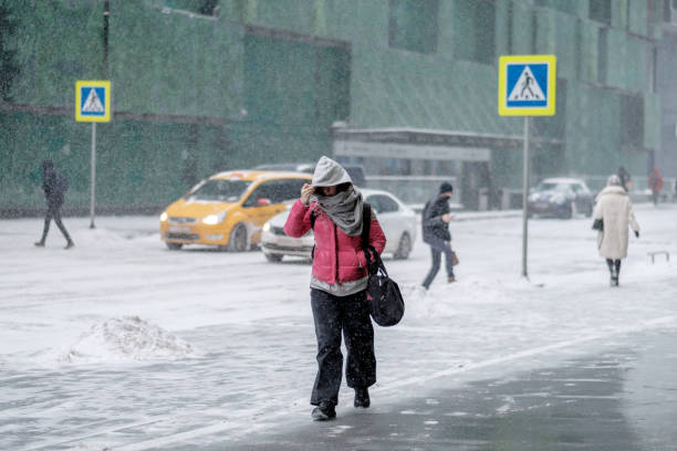 A woman walks down the street in winter, snow is falling. Moscow. Russia. February 12, 2021. City street, passer-by and snowfall. A woman walks down the street in winter and covers her face with a hood from the wind, snow is falling. Selective focus. frost face stock pictures, royalty-free photos & images