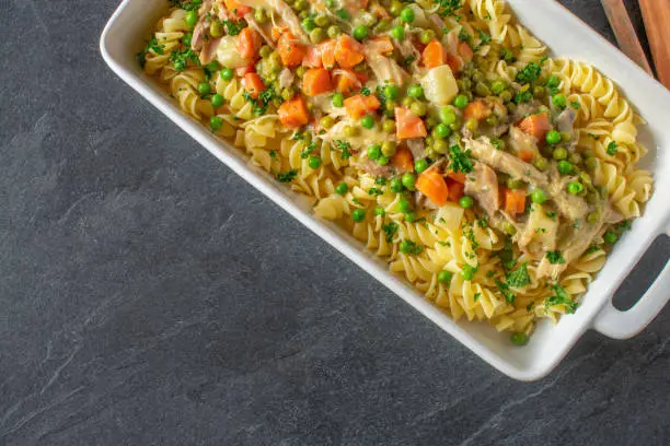 creamy chicken dish with vegetables and pasta served in a casserole on dark table from above with copy space