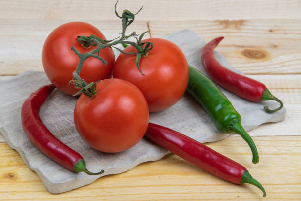 istock 3 tomatoes and 4 hot peppers on a wooden board. 1302940522