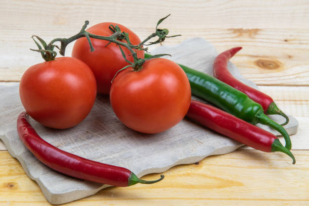 istock 3 tomatoes and 4 hot peppers on a wooden board. 1302940527
