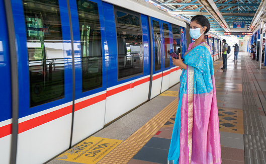 Portrait of Asian Indian female wearing protective face mask, Sari and wrapped garments waiting the subway train  arriving to the subway station.