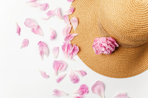 Summer, spring concept, straw braided hat, pink peony flowers and petals on white background, top view