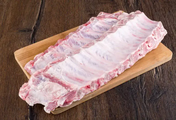 Two strips of raw pork ribs on a wooden cutting board. Close up.