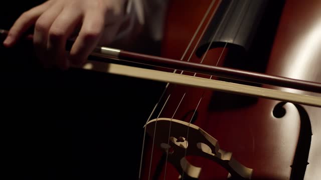 Artist plays with a bow on the strings of the cello in the darkness. Close-up musician plays with a bow of a violoncello