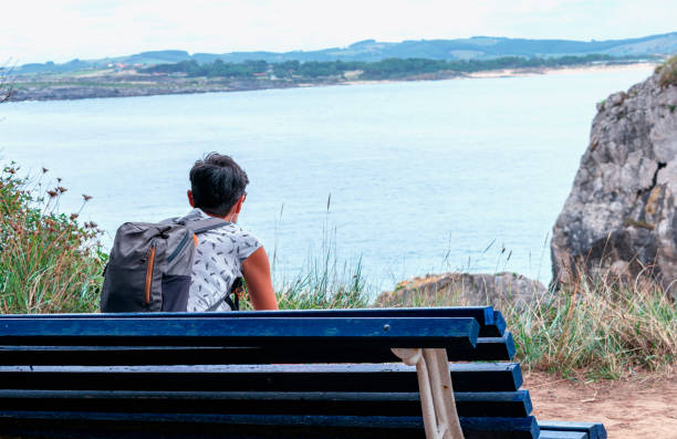 istock woman with backpack sitting on a bench looking at the sea 1302947012