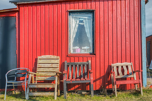 Traditional Scandinavian summerhouse or fisherman hut with a window and old chairs against the red wooden exterior made of planks