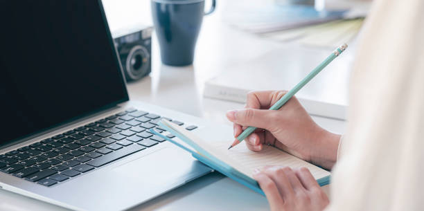 istock Closeup image of woman hand writing on notebook with pencil while working at her office desk. 1302952333