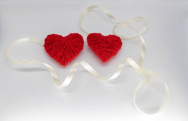istock two red knitted hearts with ribbon on a white background. happy valentines day idea. 1302952459