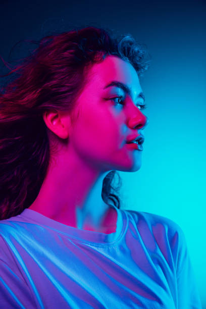 istock Caucasian woman's portrait isolated on blue studio background in multicolored neon light 1302953769