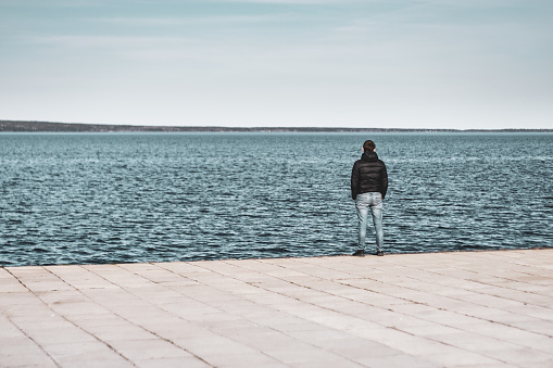 Petrozavodsk, Russia - 9 May 2019. a lonely man stands on the shore of the lake and looks into the distance. View from the back. High quality photo