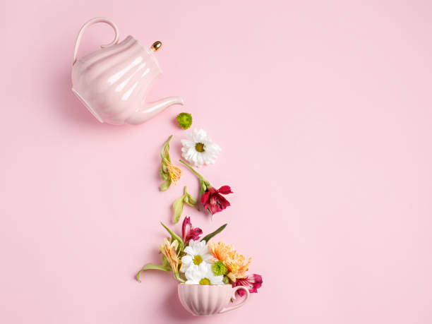 istock Creative layout with tea pot pouring fresh flowers and leaves into tea cup on pastel pink background 1302956882