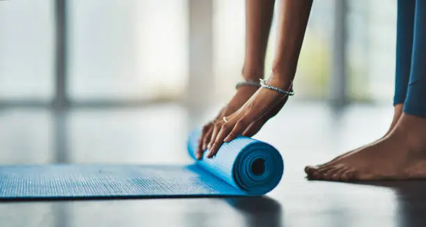 Shot of an unrecognisable woman rolling out her exercise mat in preparing for a yoga routine