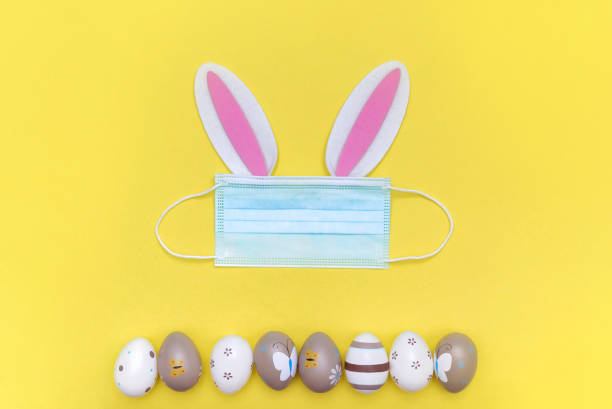 istock Easter eggs and easter bunny in protective medical mask on yellow background. Quarantine concept due to coronavirus epidemic. 1302957882