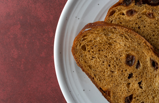 Top close view of two pumpkin raisin bread slices on a white spotted plate atop a mottled maroon table illuminated with natural lighting.