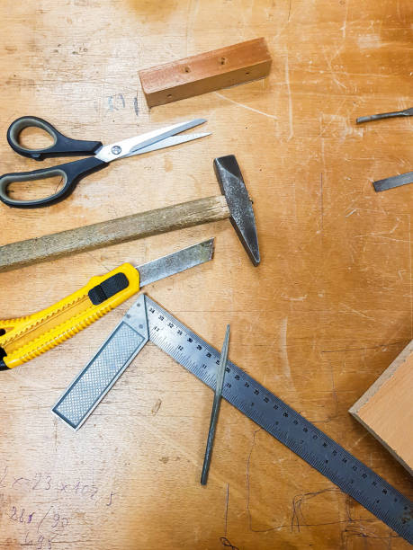 istock Various workshop tools: box cutter knife, scissors, hammer and a metal ruler on a traditional wooden work table. Crafting carpentry work space crafts creative background concept, top view 1302962805
