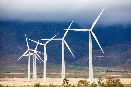 Wind farm with mountain backdrop in desert.  Sagebrush in foreground.  Angled view. Western United States.