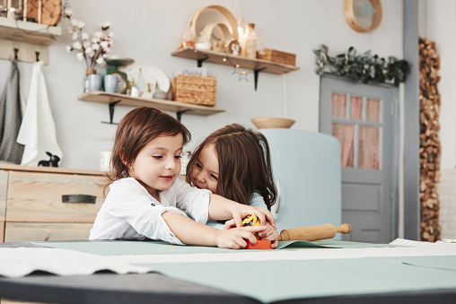 Girl on the right side smiling and wanna have fun. Two kids playing with yellow and orange toys in the white kitchen.