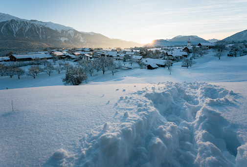 Snow covered rural winter landscape during sunset with sun star between alpine mountains, Wildermieming, Tyrol, Austria