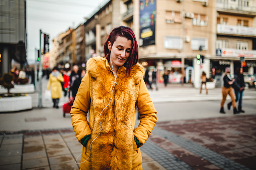 Beautiful young woman in yellow jacket listening music and walking downtown.