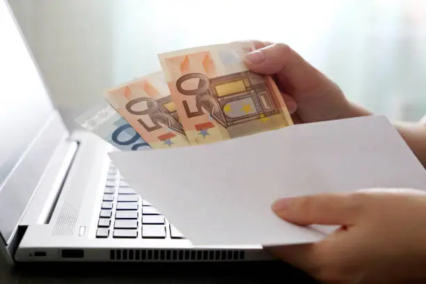 Woman pulls money out of an envelope on laptop background, wages, bonus or bribe concept