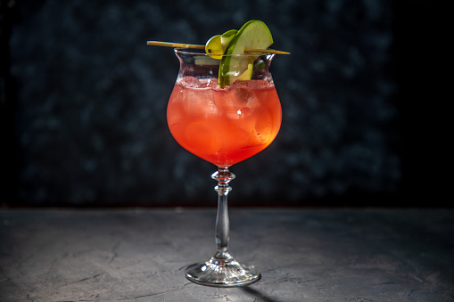 Red cocktail in wine glass with grape and apple slices on cocktail stick