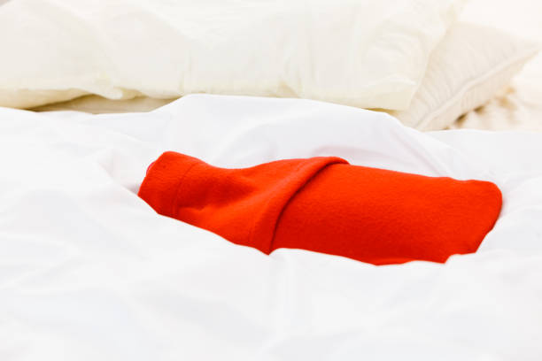 istock Warm red hot water bottle on white bedding 1302977182