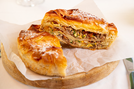 Traditional meat pie brought to Serbia by Turks becoming national food of the region, served on round wooden board