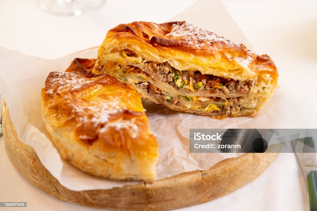 Burek with minced meat and other ingredients cut in half Traditional meat pie brought to Serbia by Turks becoming national food of the region, served on round wooden board Ground Beef Stock Photo