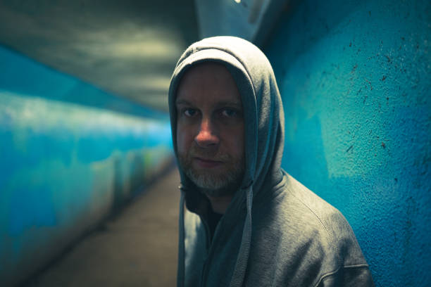 Sideview head shot of a black man with hood hiding his face and showing only nose and chin with beard, in the shadow, on black background, horizontal.