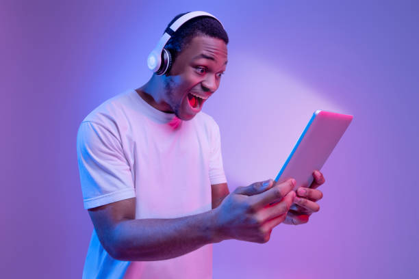 istock Online Offer. Black Guy In Headphones Holding Digital Tablet With Glowing Screen 1302978435