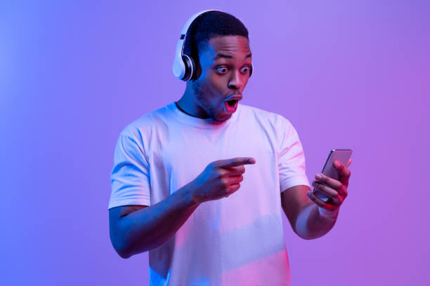 istock Mobile Offer. Shocked Black Guy Looking At Smartphone With Excitement, Neon Light 1302978970
