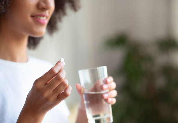 Smiling woman taking white round pill, holding water glass in hand Smiling woman taking white round pill, holding water glass in hand. Happy young female taking supplement, daily vitamins for hair, skin, body, natural beauty and healthy lifestyle, free space, cropped birth control pill stock pictures, royalty-free photos & images