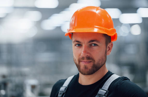 retrato del trabajador industrial masculino en el interior de la fábrica. joven técnico con sombrero duro naranja - manual worker portrait helmet technology fotografías e imágenes de stock