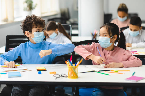 istock Diverse pupils wearing surgical face masks greeting and bumping elbows 1302981377