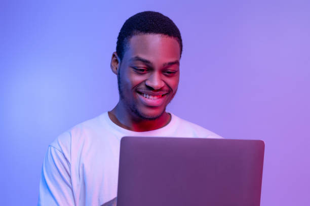 istock Handsome Smiling Black Programmer Guy Working Online On Laptop In Neon Light 1302981398