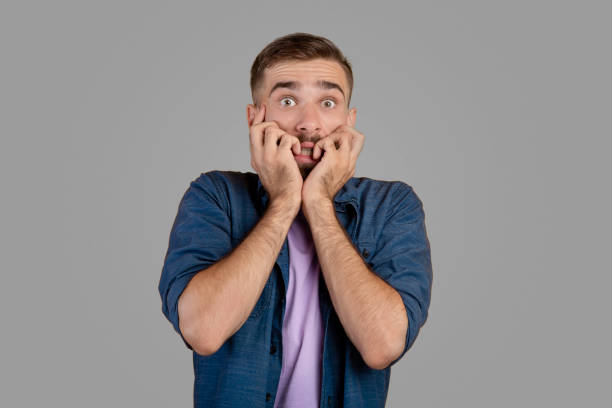 istock Scared Caucasian guy biting his nails in terror over grey studio background. Expressing negative emotions concept 1302982874