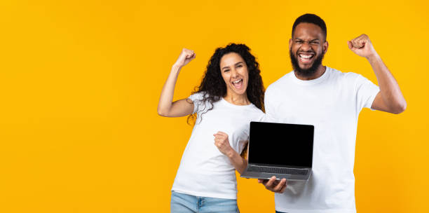 istock Multiracial Couple Showing Laptop Screen Gesturing Yes Over Yellow Background 1302984568
