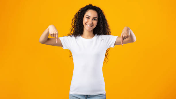 istock Happy Curly Woman Pointing Fingers Down Posing Over Yellow Background 1302985756
