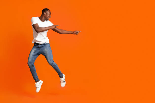istock Millennial african american man pointing at copy space while jumping 1302986079