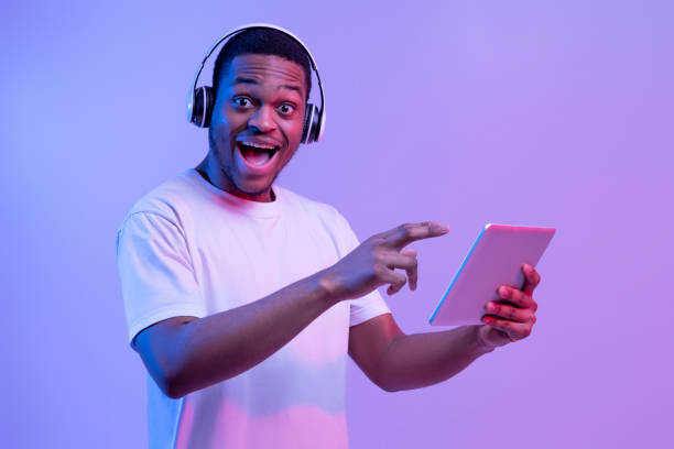 istock Check This App. Excited Black Man In Headphones Pointing At Digital Tablet 1302986093
