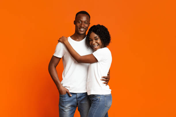 istock Joyful black couple in love hugging on orange 1302987773