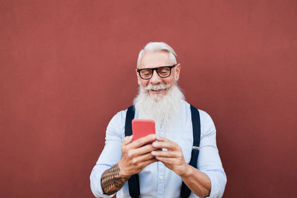 istock Senior hipster man using mobile phone outdoors with red wall in background - Focus on face 1302987870