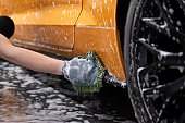 Manual car wash worker cleaning orange sports car