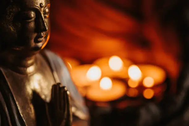 Photo of Close up of a buddha figurine seen slightly from the side in front of lit candles