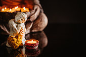 Small buddha of compassion figurine with a lit candle and a golden heart in front of the lower part of a bigger buddha holding lit candles