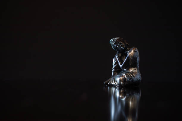 Small black buddha of compassion figurine on dark background with reflection and copy space. For mindfulness and wisdom concepts. Copy space on the right side. Selective focus and added grain. Part of an E+ and S+ series.