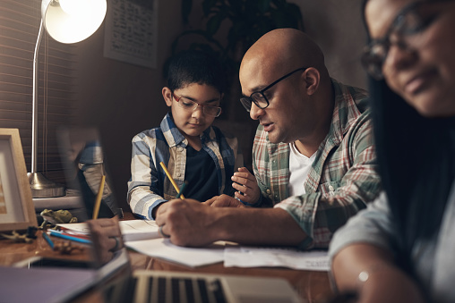 Shot of an adorable little boy completing a school assignment with his father at home