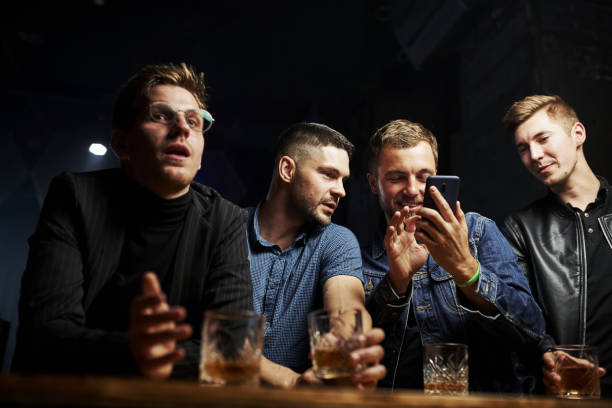 istock Front view. Friends resting in the pub with alcohol in hands. Having conversation 1302991272